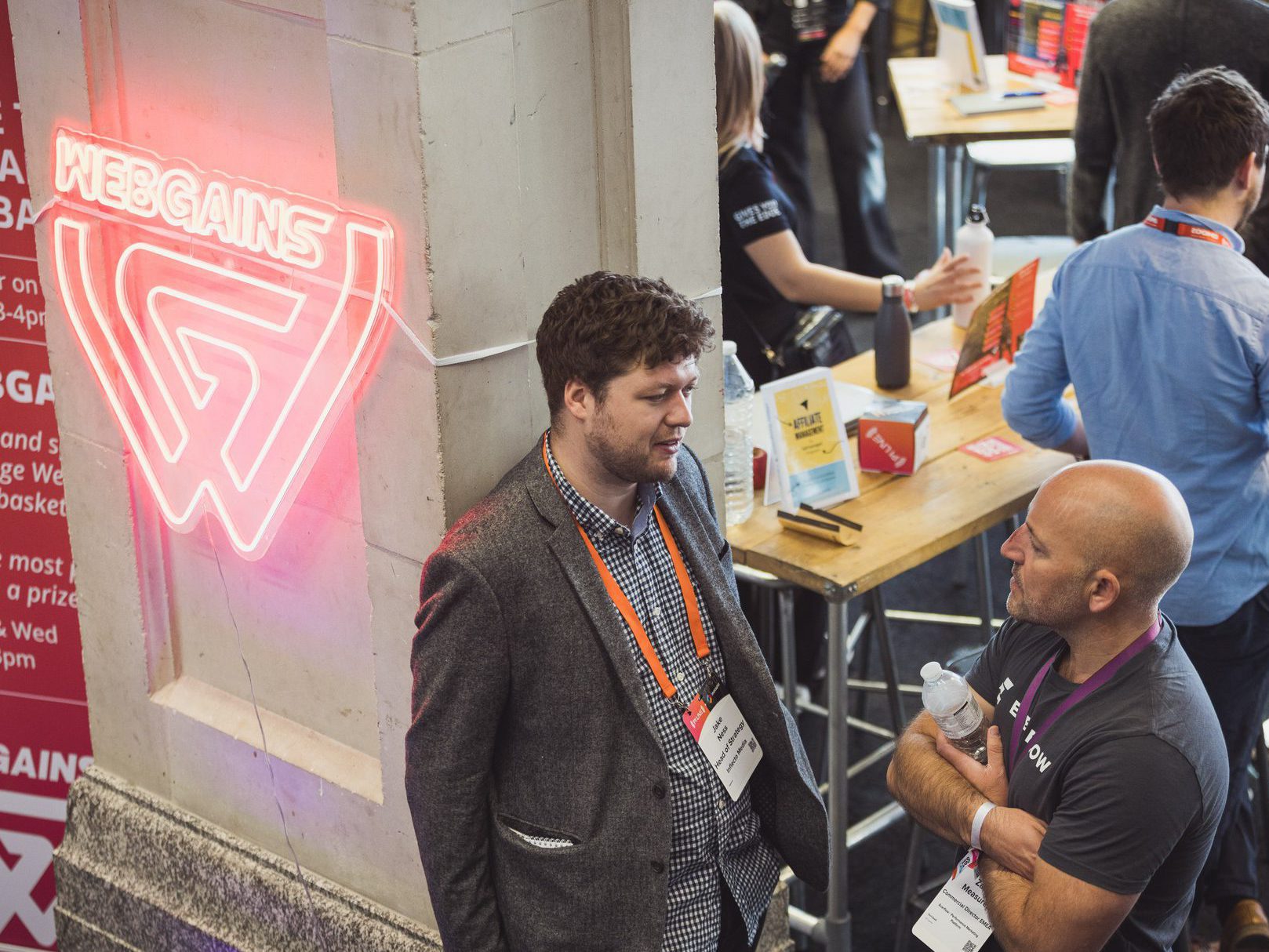 Image showing two men talking by a neon Webgains sign at a trade show.